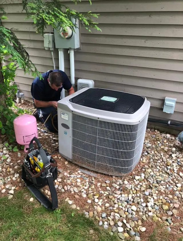 A City technician servicing an outdoor residential air conditioning condenser unit.