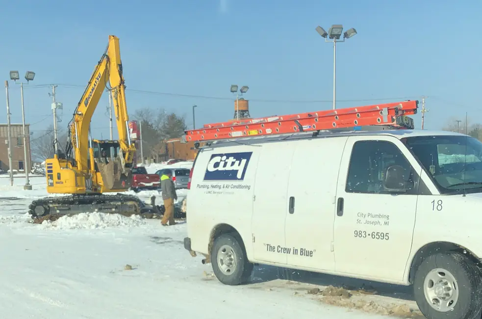 A branded City Plumbing van parked at a commercial excavation site beside a working excavator.
